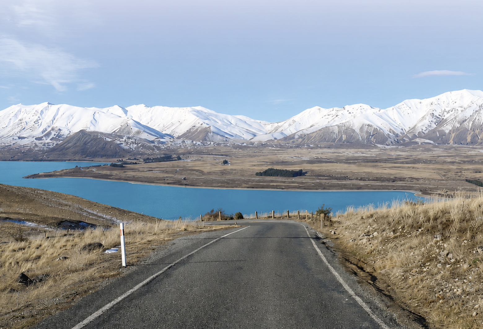 The image depicts a serene, snow-covered mountain landscape with a clear blue lake, a desolate, winding road, and a calm, cloudy sky overhead.AI-generated content may be incorrect.